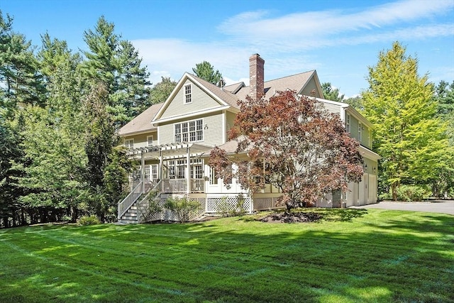 rear view of property featuring driveway, a pergola, a yard, a garage, and a chimney