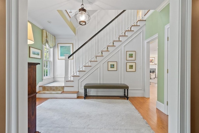 foyer featuring a decorative wall, wood finished floors, stairs, and ornamental molding