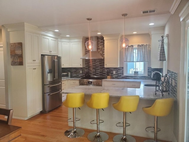 kitchen featuring sink, hanging light fixtures, stainless steel appliances, wall chimney range hood, and a breakfast bar area