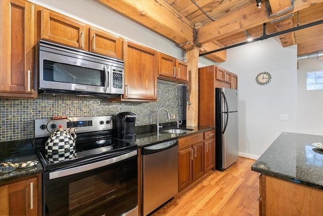 kitchen with appliances with stainless steel finishes, a sink, brown cabinets, light wood-style flooring, and tasteful backsplash