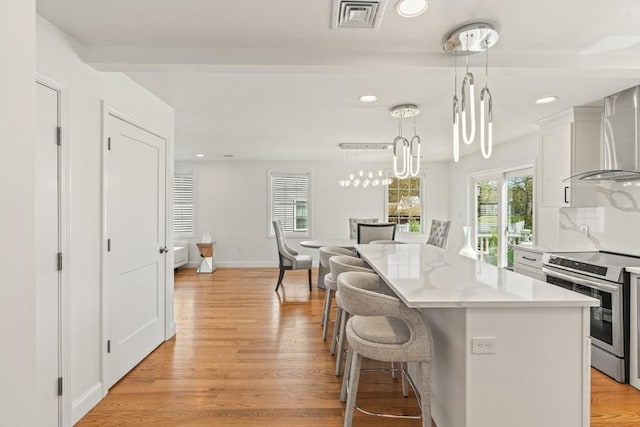 kitchen featuring visible vents, a kitchen breakfast bar, wall chimney exhaust hood, white cabinetry, and stainless steel range with electric cooktop