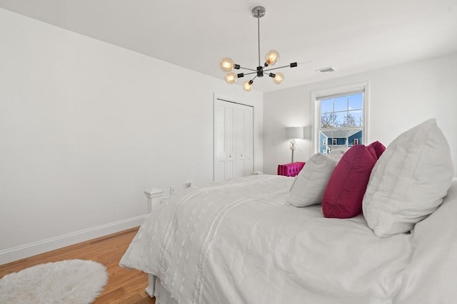 bedroom featuring visible vents, a closet, baseboards, light wood-type flooring, and a chandelier