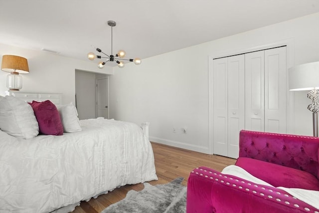 bedroom featuring an inviting chandelier, baseboards, wood finished floors, visible vents, and a closet
