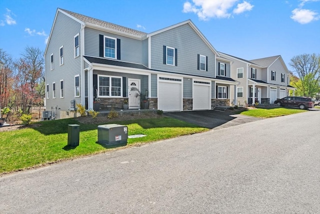 multi unit property with a garage, stone siding, driveway, and a front yard