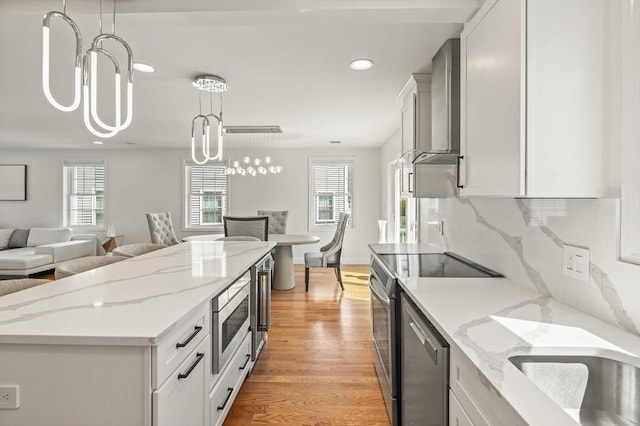 kitchen with light wood-style floors, open floor plan, wall chimney range hood, plenty of natural light, and appliances with stainless steel finishes