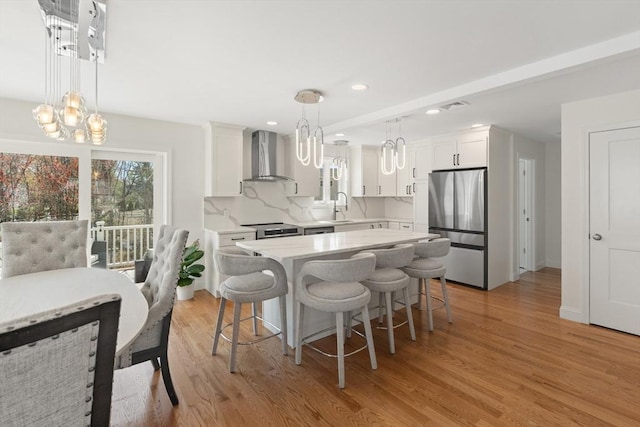 kitchen featuring wall chimney range hood, stainless steel appliances, a notable chandelier, and white cabinetry