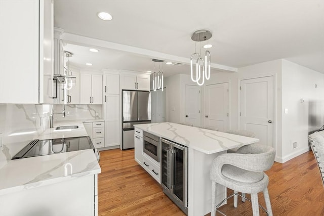 kitchen featuring white cabinets, appliances with stainless steel finishes, a sink, beverage cooler, and a kitchen island