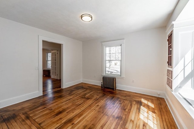 spare room with radiator heating unit, a wealth of natural light, baseboards, and hardwood / wood-style floors