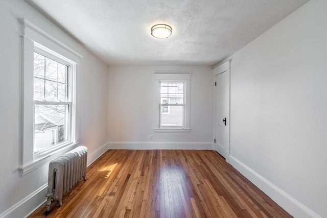 unfurnished room featuring a textured ceiling, radiator heating unit, wood-type flooring, and baseboards