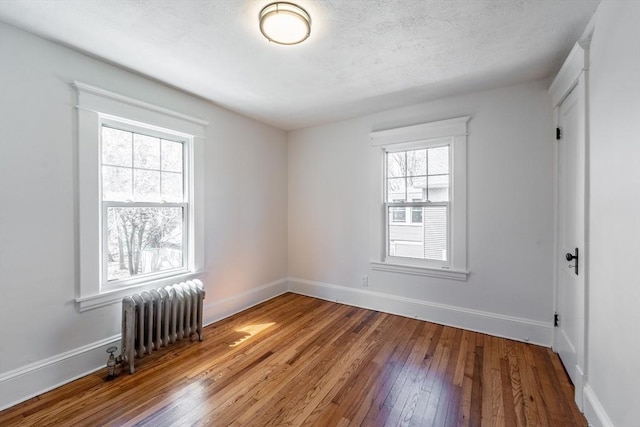unfurnished room featuring hardwood / wood-style floors, radiator heating unit, and baseboards