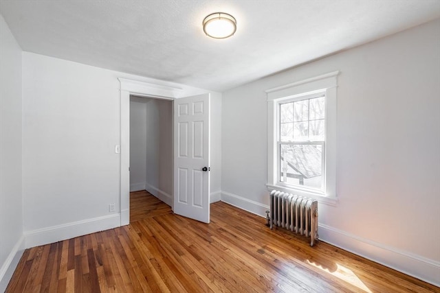 unfurnished bedroom with radiator, wood finished floors, and baseboards