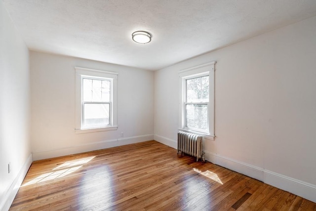 spare room featuring a wealth of natural light, light wood finished floors, radiator, and baseboards