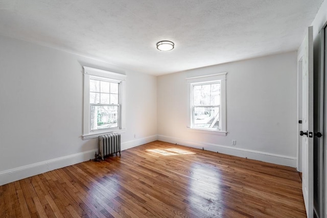 unfurnished room with radiator heating unit, a wealth of natural light, wood finished floors, and baseboards