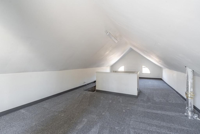 additional living space featuring dark colored carpet, baseboards, and vaulted ceiling