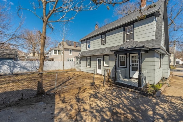 rear view of property featuring fence, a chimney, and a shingled roof