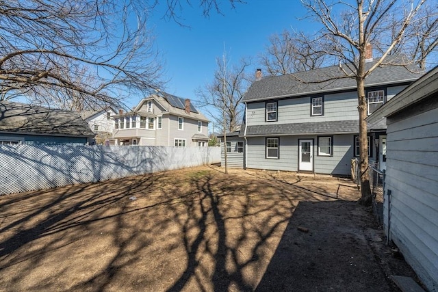 rear view of property with a chimney, fence, and roof with shingles