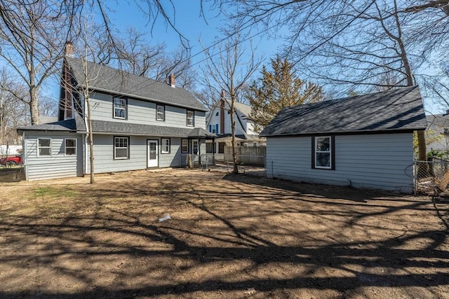 rear view of property with an outdoor structure, a chimney, fence, and roof with shingles