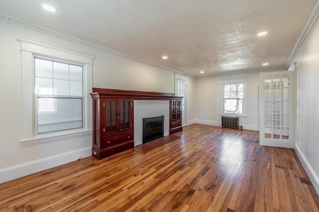 unfurnished living room featuring baseboards, radiator, hardwood / wood-style floors, and a fireplace with flush hearth