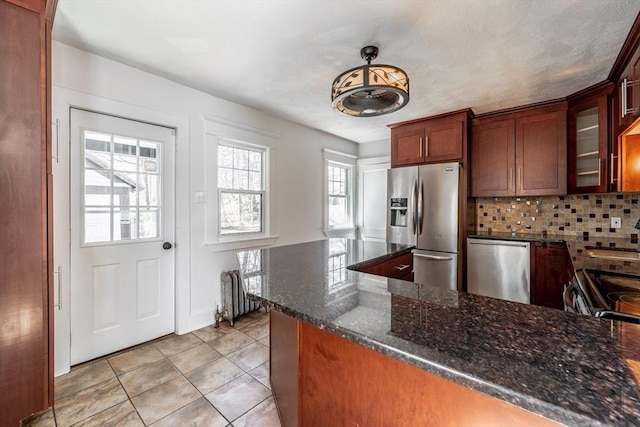 kitchen featuring glass insert cabinets, backsplash, light tile patterned flooring, dark stone counters, and appliances with stainless steel finishes