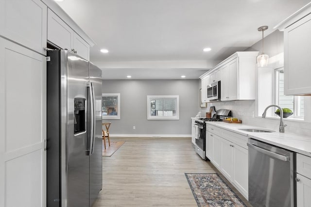 kitchen featuring appliances with stainless steel finishes, white cabinets, decorative backsplash, hanging light fixtures, and light wood-type flooring