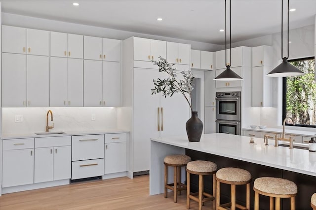48 Sherburne Rd, Lexington, MA 02421 - kitchen featuring stainless steel double oven, a sink, light countertops, light wood-type flooring, and pendant lighting
