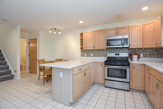 kitchen featuring light brown cabinetry, a peninsula, appliances with stainless steel finishes, and backsplash