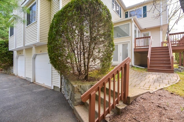 view of property exterior with a garage, a deck, stairway, french doors, and driveway