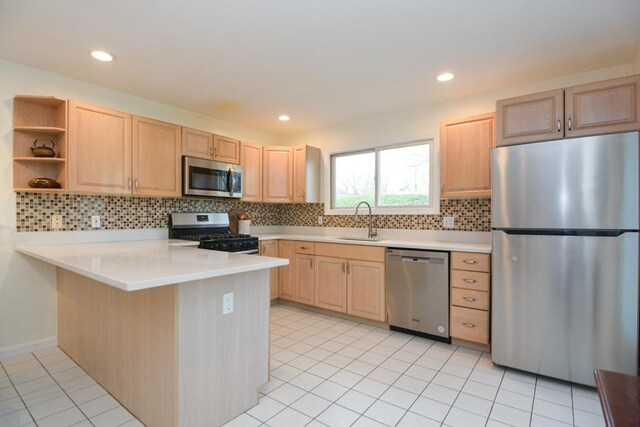 kitchen with a sink, a peninsula, light brown cabinets, and stainless steel appliances