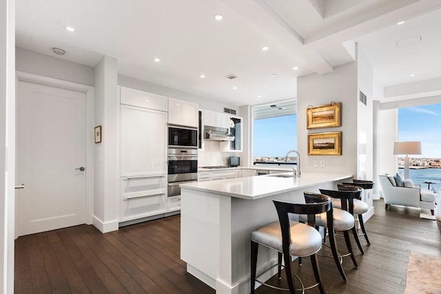 kitchen with stainless steel appliances, a sink, a peninsula, a warming drawer, and dark wood finished floors