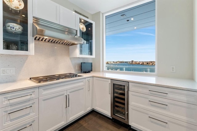 kitchen with beverage cooler, under cabinet range hood, stainless steel gas stovetop, and white cabinets