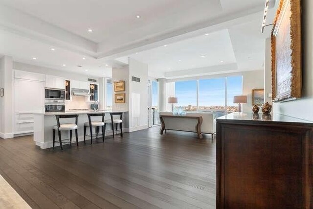 living area with dark wood-type flooring, a raised ceiling, baseboards, and recessed lighting