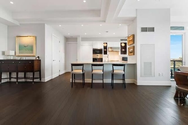 kitchen with dark wood finished floors, a kitchen breakfast bar, white cabinets, baseboards, and a peninsula
