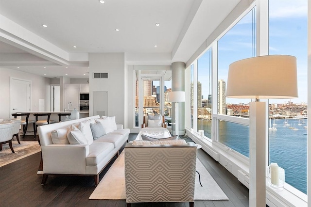 living area featuring dark wood-type flooring, a water view, and recessed lighting