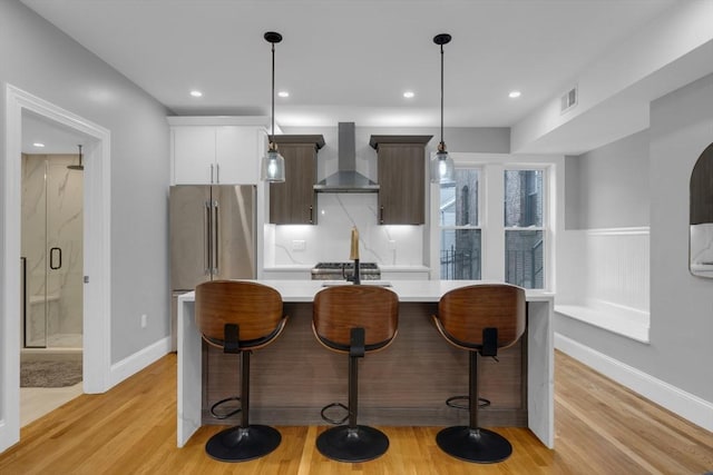 kitchen with white cabinets, wall chimney exhaust hood, a kitchen bar, hanging light fixtures, and high end refrigerator