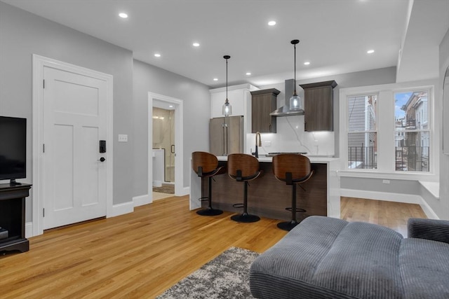 kitchen with light wood-type flooring, a breakfast bar, high quality fridge, wall chimney exhaust hood, and dark brown cabinets