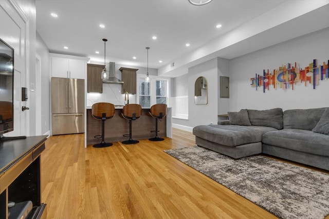 living room with sink, electric panel, and light hardwood / wood-style flooring