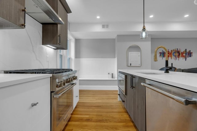 kitchen featuring stainless steel appliances, sink, wall chimney exhaust hood, light hardwood / wood-style flooring, and pendant lighting