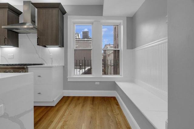 kitchen with wall chimney range hood, light hardwood / wood-style floors, stainless steel gas cooktop, stove, and dark brown cabinetry