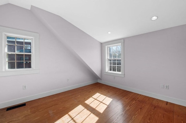 additional living space featuring vaulted ceiling, plenty of natural light, baseboards, visible vents, and wood finished floors