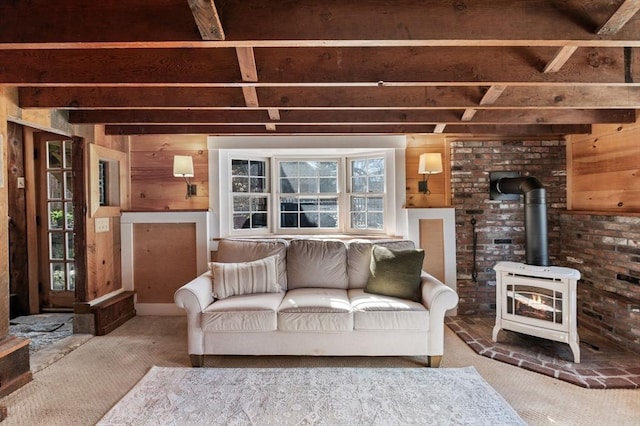 carpeted living area featuring a wood stove, wooden walls, and beamed ceiling