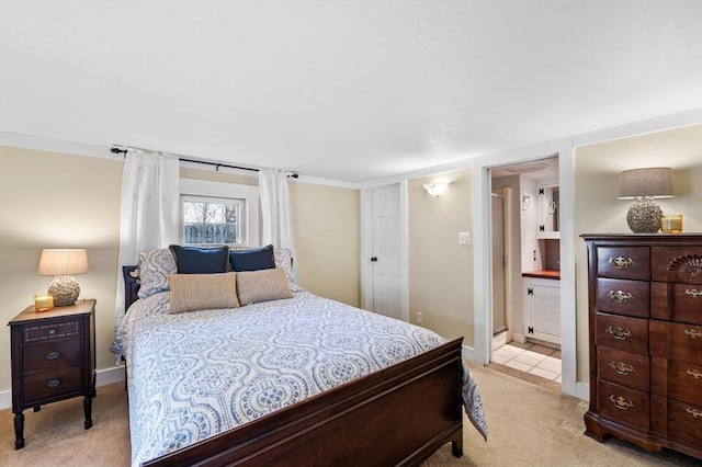 bedroom featuring ensuite bath, light carpet, and baseboards