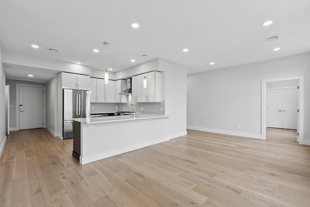 kitchen featuring white cabinetry, wall chimney exhaust hood, visible vents, and stainless steel refrigerator