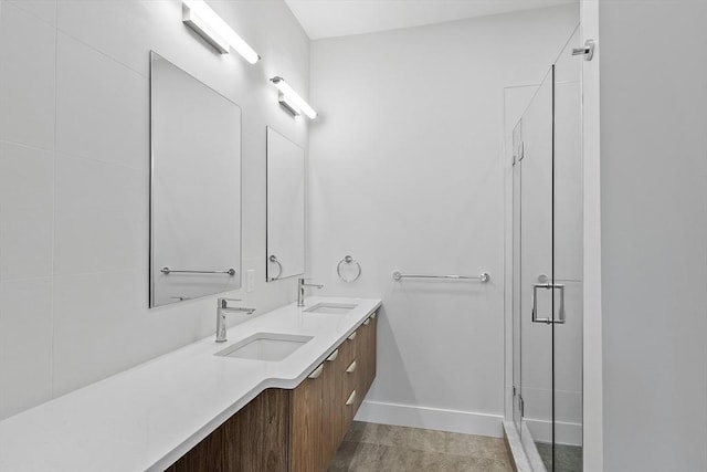 full bath featuring a sink, baseboards, a stall shower, and double vanity