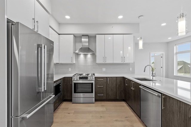 kitchen featuring modern cabinets, a sink, stainless steel appliances, dark brown cabinetry, and wall chimney exhaust hood