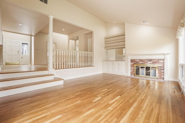 25 Hopewell Farm Rd Unit 25, Natick, MA 01760 - unfurnished living room featuring lofted ceiling, light wood-style flooring, ornate columns, a brick fireplace, and stairway