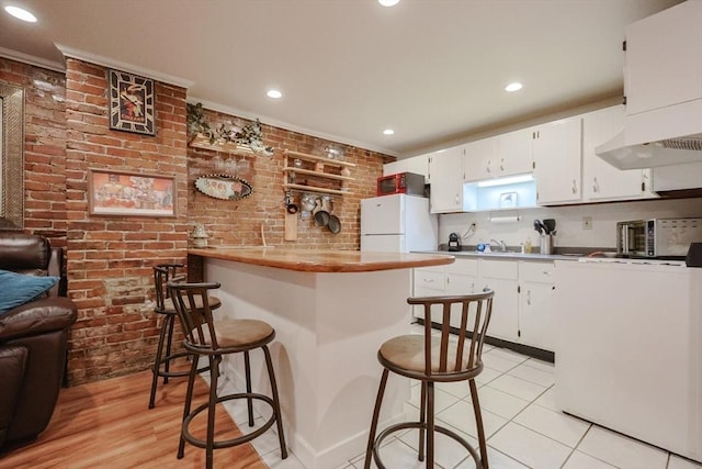 33 Inman St Unit 1B, Cambridge, MA 02139 - kitchen with a kitchen bar, white cabinets, a peninsula, brick wall, and recessed lighting