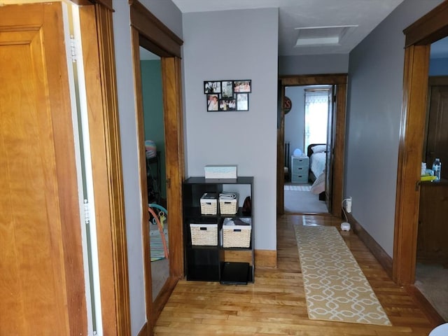 hall with baseboards, light wood-style floors, and attic access