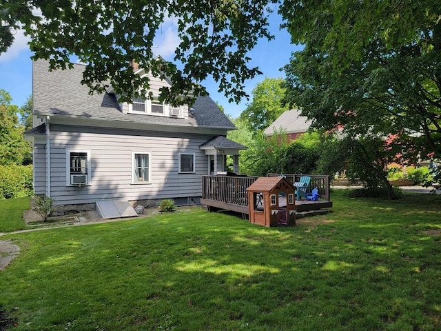 rear view of house featuring a lawn, cooling unit, a wooden deck, and roof with shingles