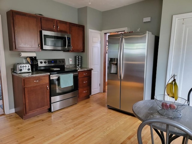 kitchen featuring a toaster, dark stone counters, stainless steel appliances, and light wood-style floors