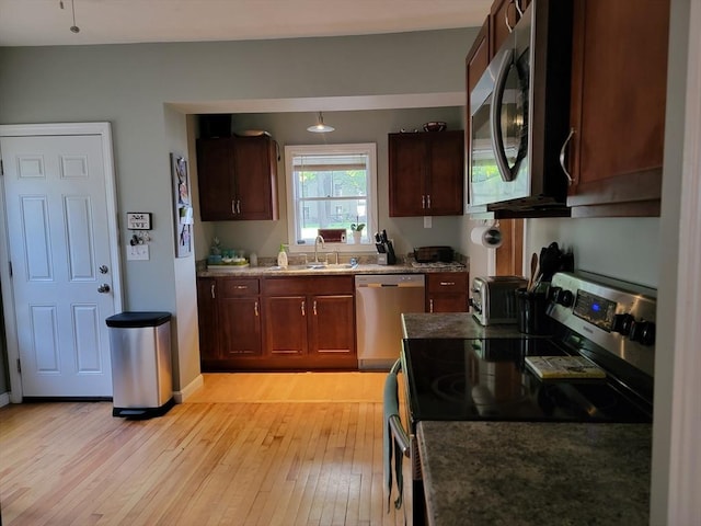 kitchen featuring light wood finished floors, a toaster, light stone counters, stainless steel appliances, and a sink